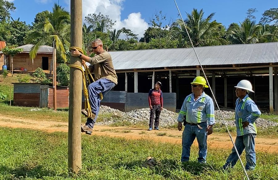 SMECO lineworker climbs a pole using Guatemalan equipment while local lineworkers watch