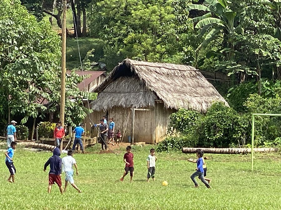 Children in Santa Isabel playing soccer in front of house with thatch roof
